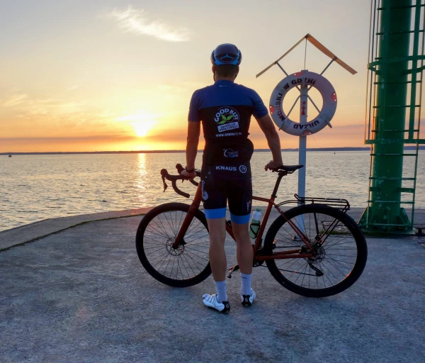 Gravelbiker kijkt op een pier in de jachthaven van Tolkmicko naar de zon die in de Vistula-lagune zakt